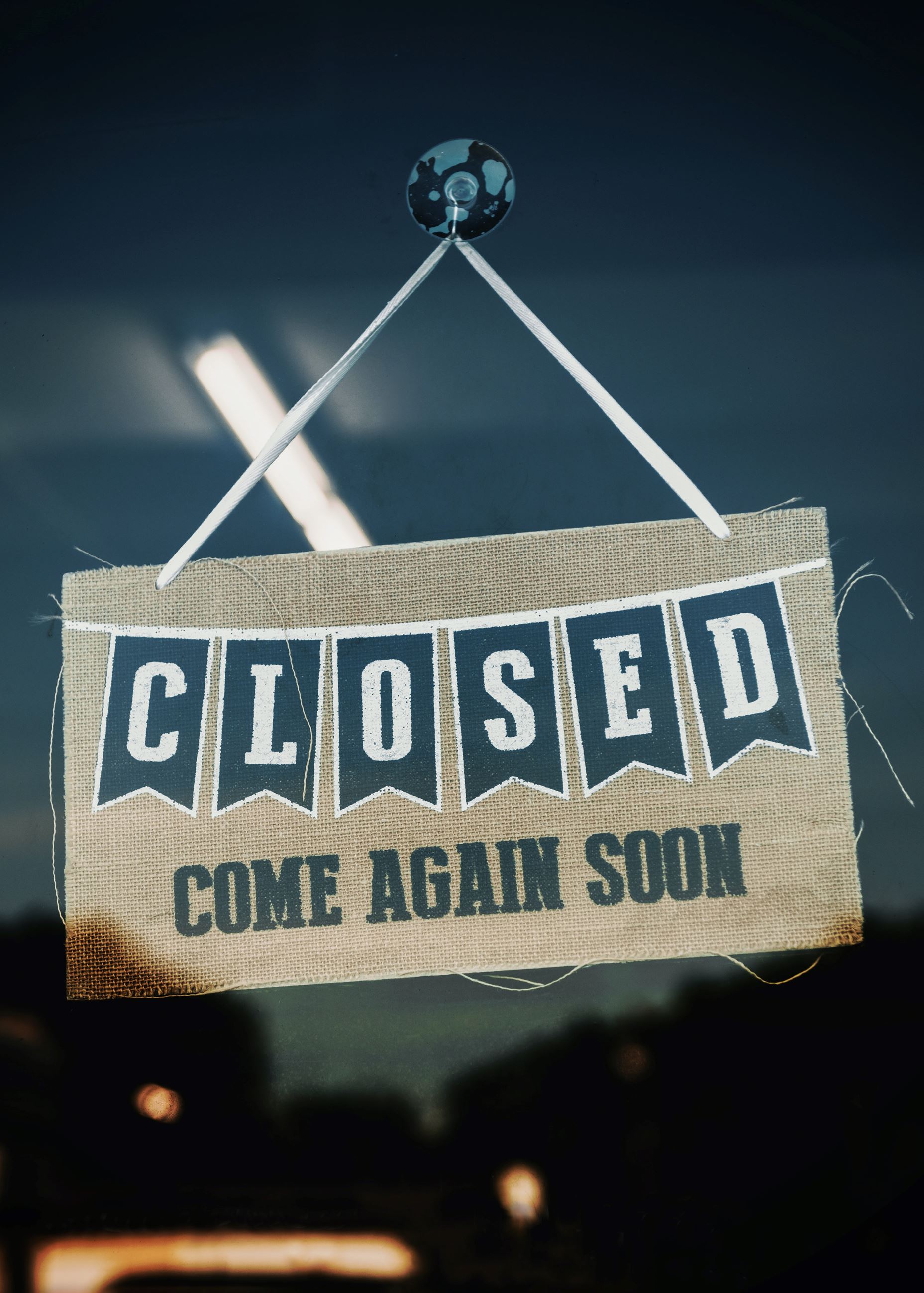 Sign Hanging From a Glass Door says Closed Come Again Soon