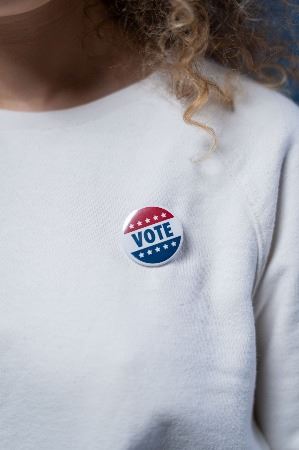 Woman with curly hair with a vote button on a white sweater