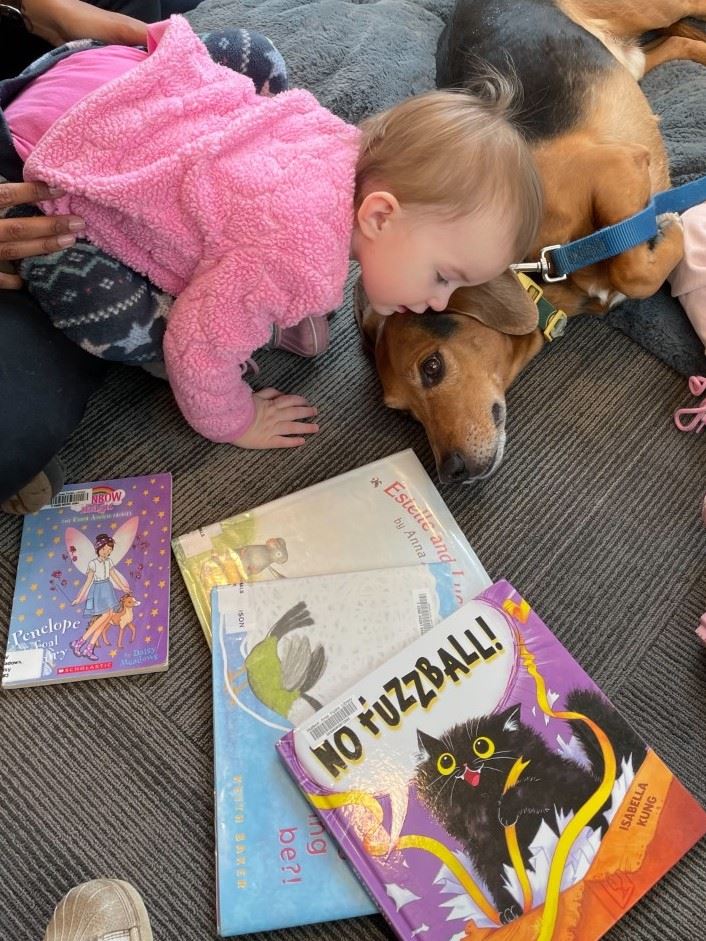 Image of a child laying on the floor with books and a medium sized dog beside them. 