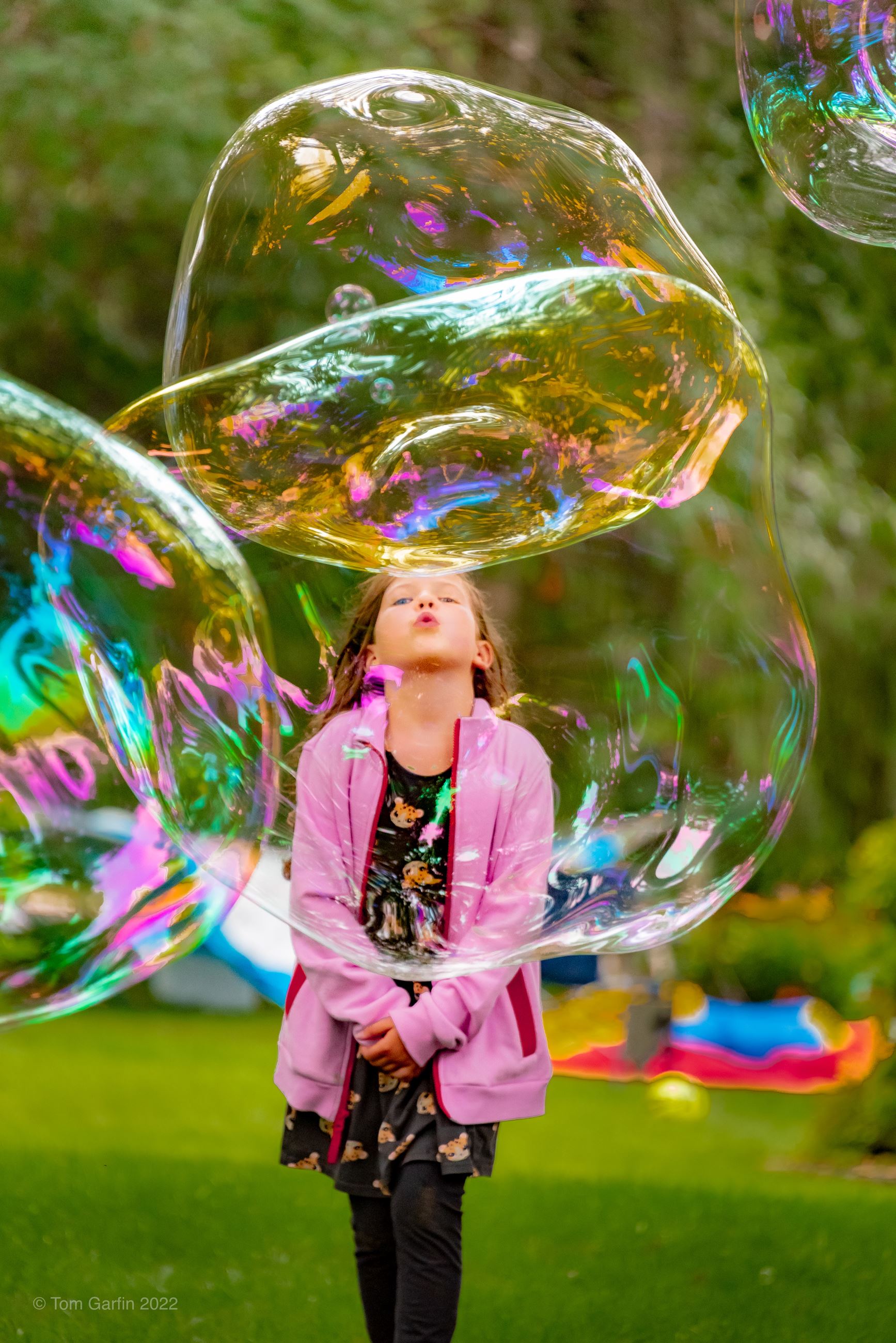 Child in pink sweatshirt blowing bubbles.