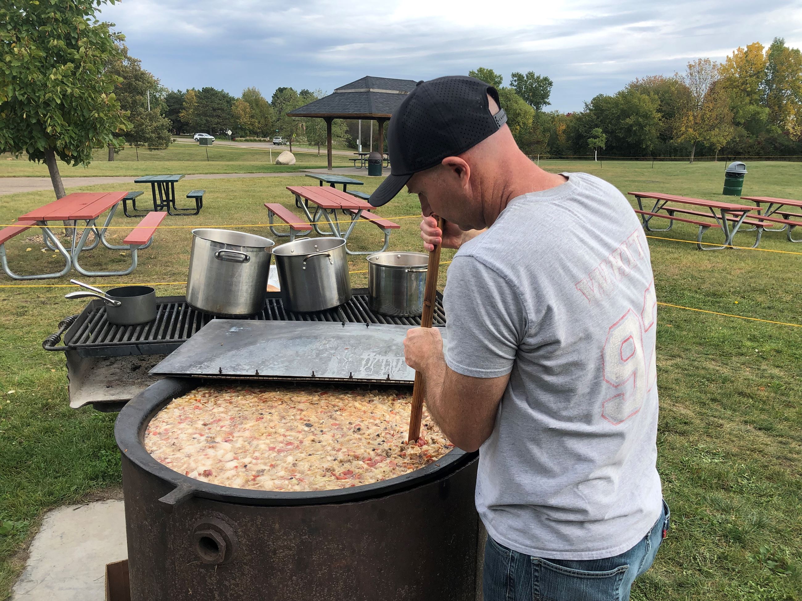 Man stirring a large pot of booyah outside.